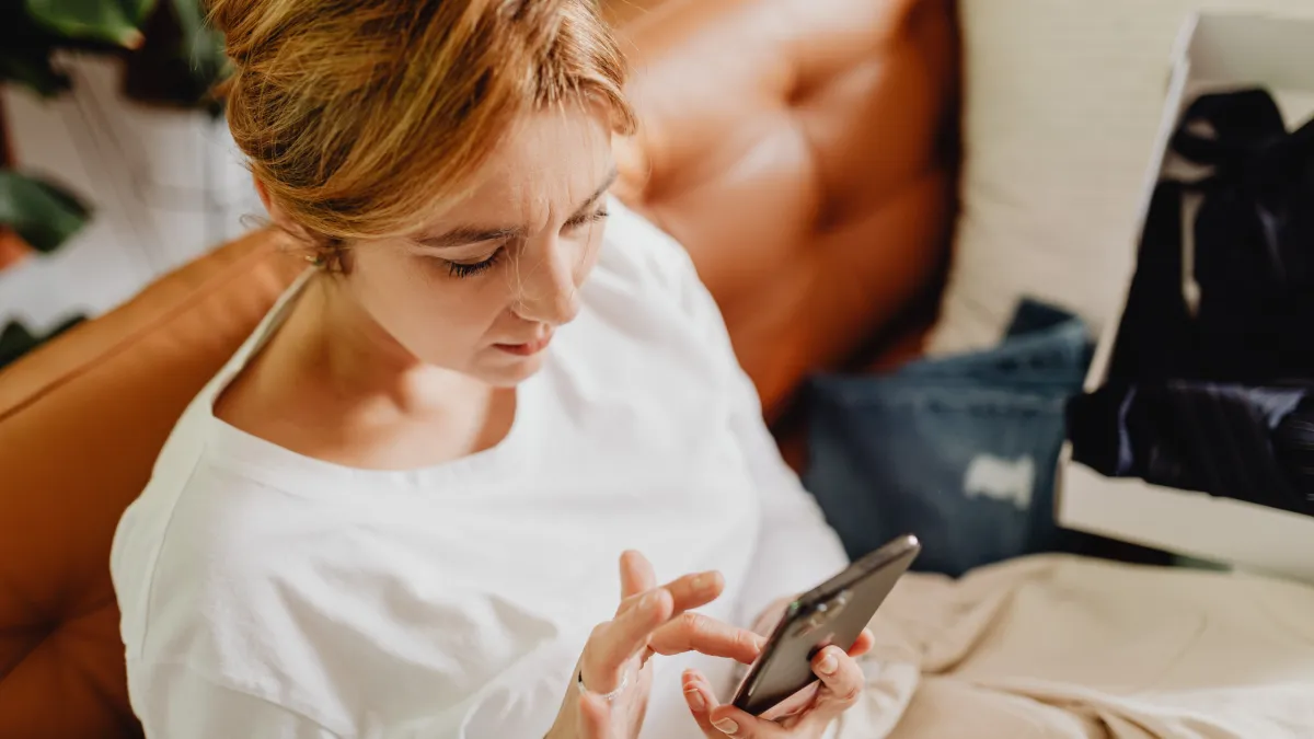 Woman sitting on a sofa using her smartphone, appearing to research or look for information online.