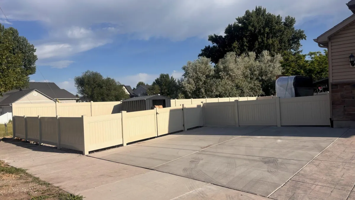 tan vinyl fence in a yard with a concrete driveway