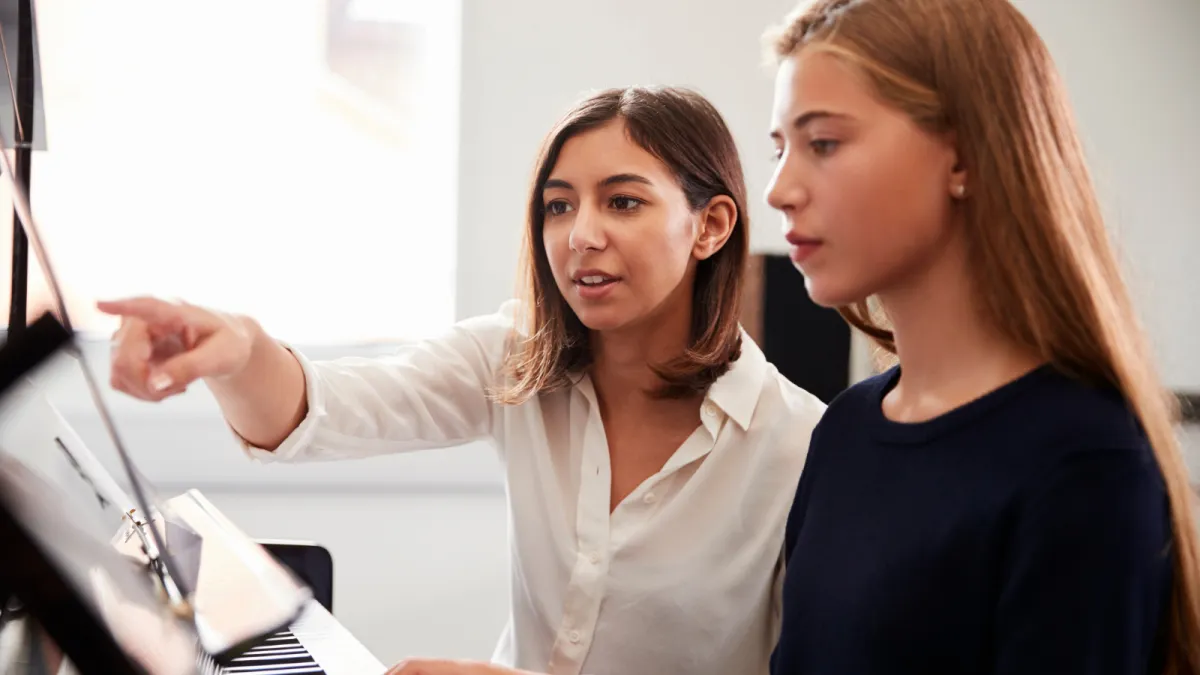 An adult, dressed in a colorful long sleeve and eyeglasses, sits attentively at a sleek digital keyboard, their fingers moving gracefully over the keys. The soft glow of a tilt light bathes the scene, casting an inviting, warm ambiance around them.