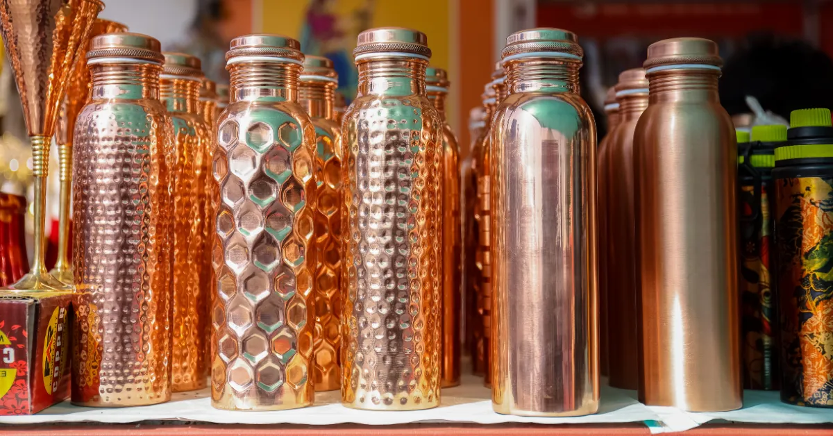 Pure Ayurvedic copper water bottles displayed in a row featuring hammered, smooth, and hexagonal honeycomb textures.