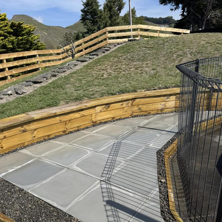 Timber retaining walls and grey paved walkway on sloped garden, showcasing landscaping services in Hastings, Hawke's Bay by Mitch's Maintenance