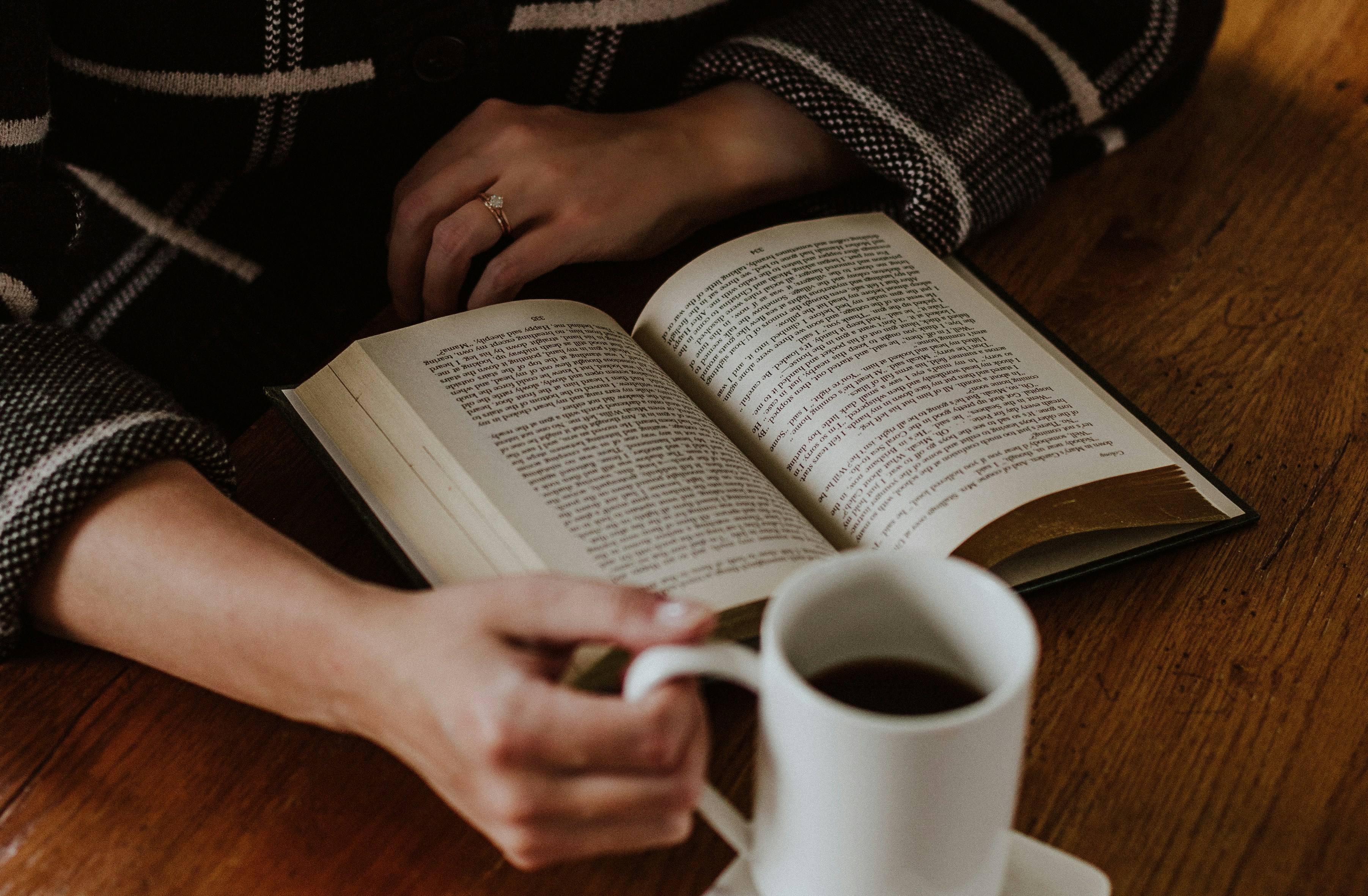Hand holding a warm cup of coffee beside an open novel