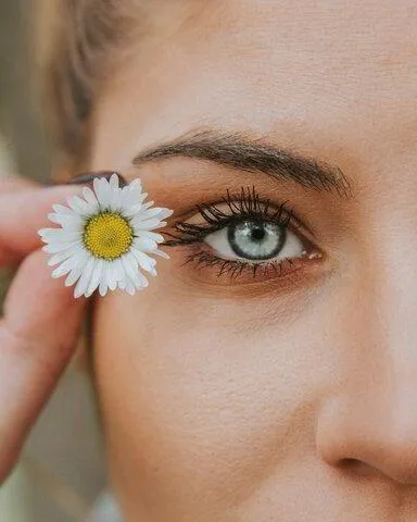 woman holding a daisy flower up to her blue eye