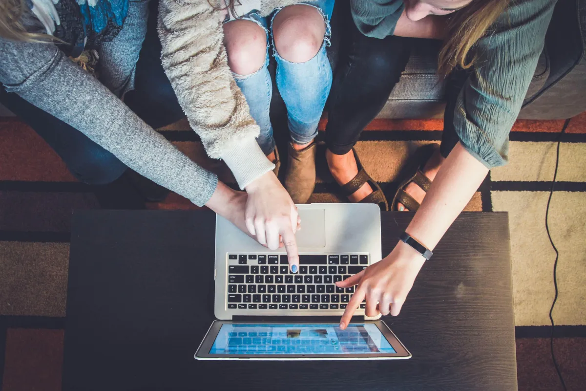 Three girls pointing at  the laptop screen which is on the table