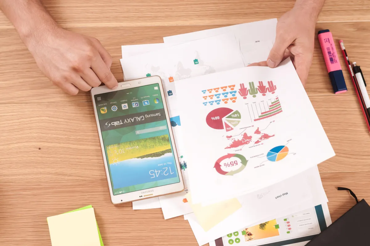 A person is looking at the paper with some statistics which is on the table and using the mobile