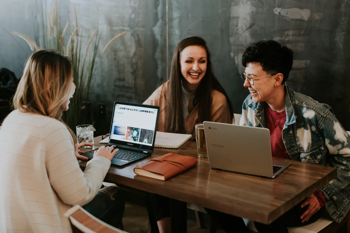 Three people sitted around the table and talking and laughing while working on the two laptops placed on the table