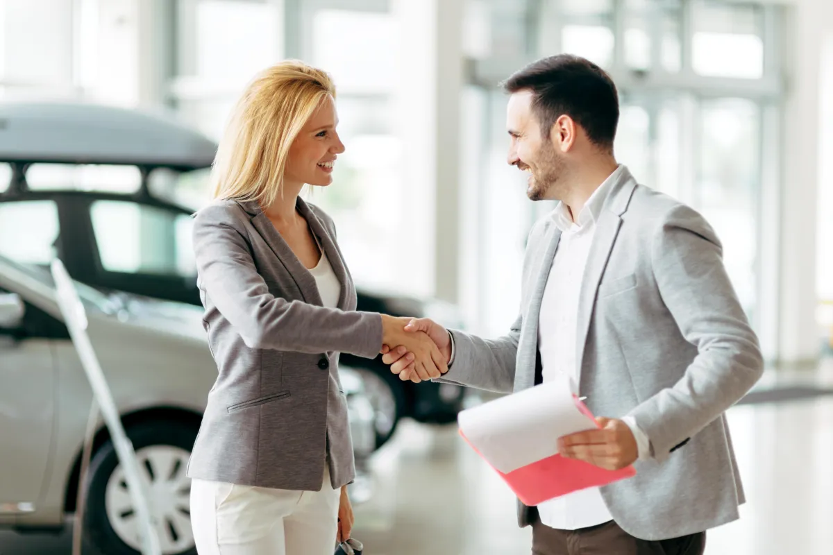 A lady and a man shaking hands the parking slot and the man having some documents in his other hand