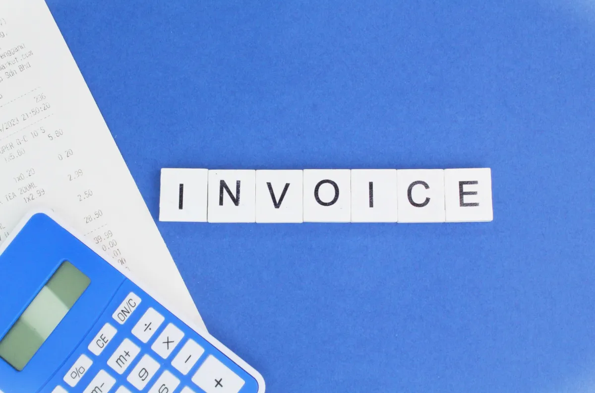 The word invoice is created using the blocks of letter and a calculator along with a invoice is placed next to it