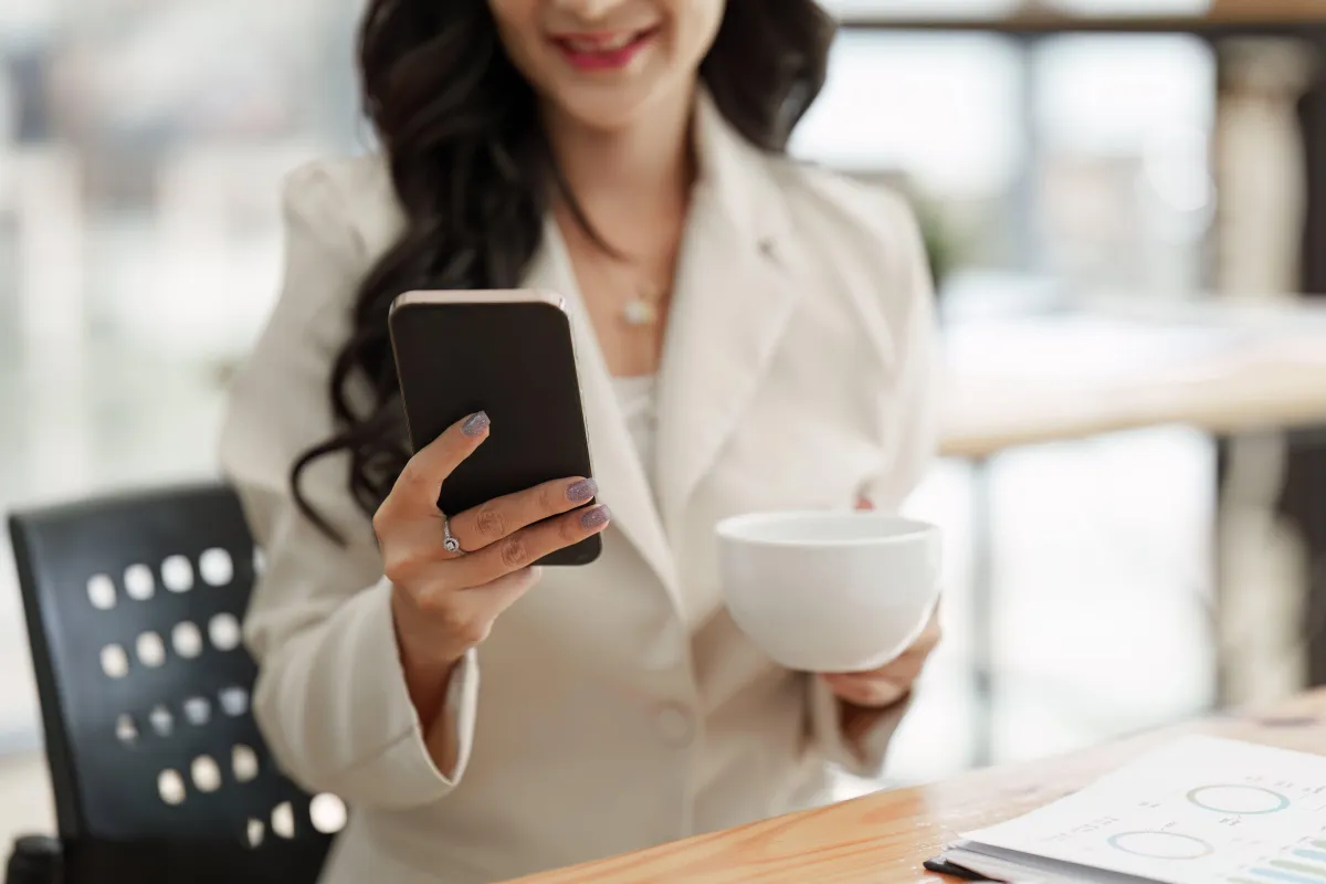 A lady standing and looking at the phone while having coffee
