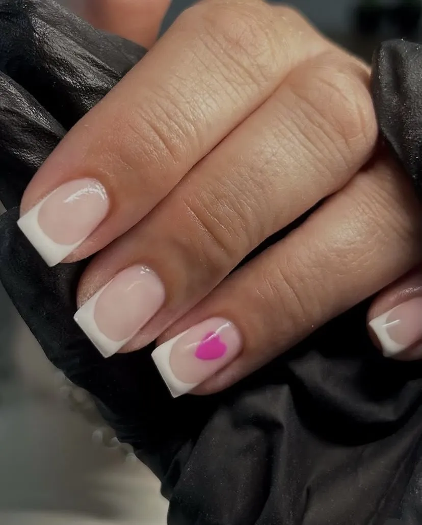 White French tips with a bright pink heart accent, by Beauty by Amy