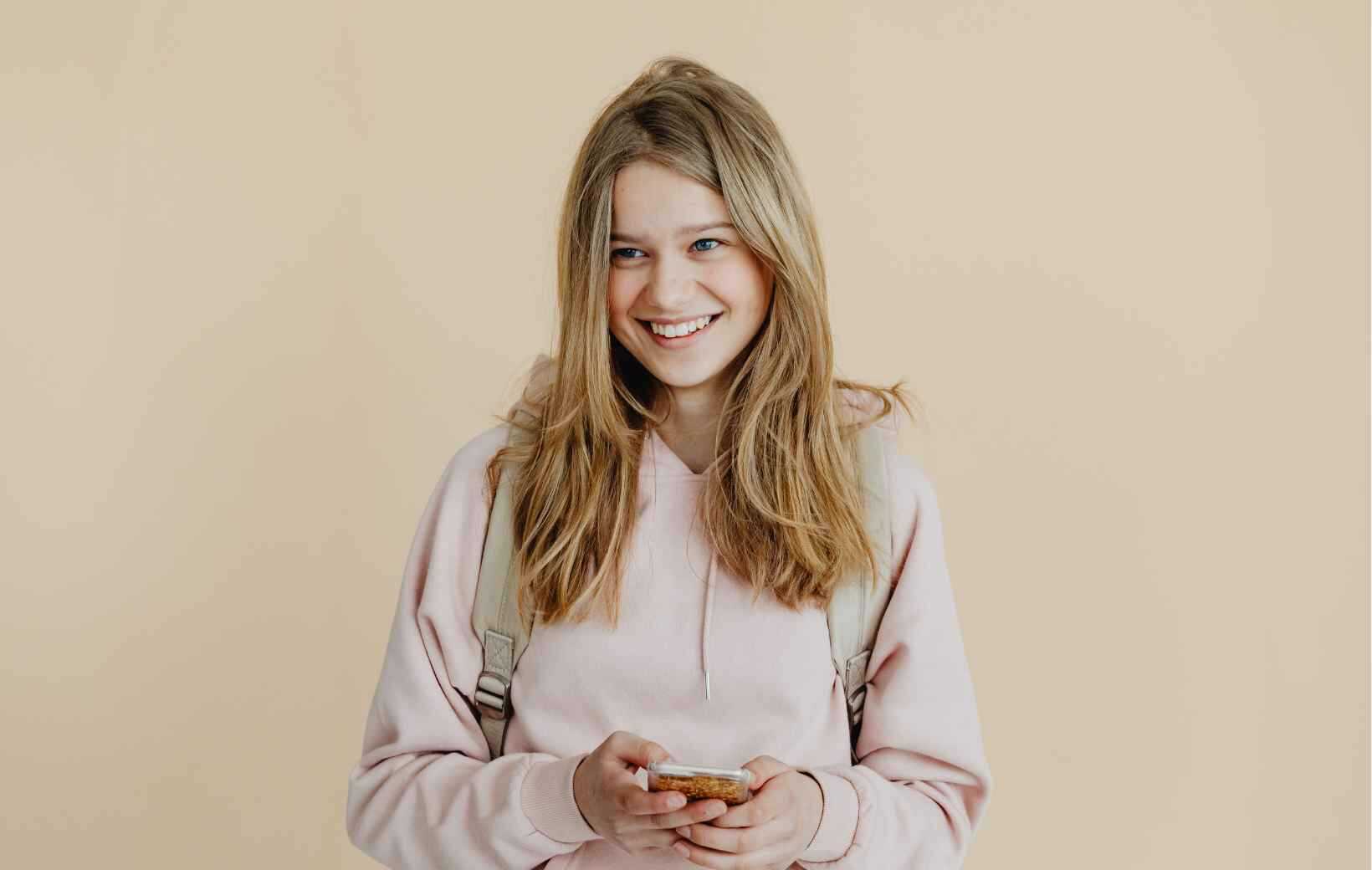 Jugendliche im beigen Hoody liest ihre Nachrichten auf dem Handy.