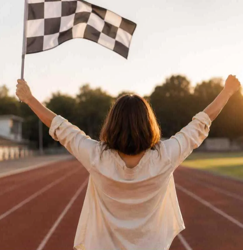 Mental Coach für jugendliche Sportler Kerstin Waterman mit dem Rücken zur Kamera. Sie seht auf einer Laufbahn und hält eine Zielflagge hoch.