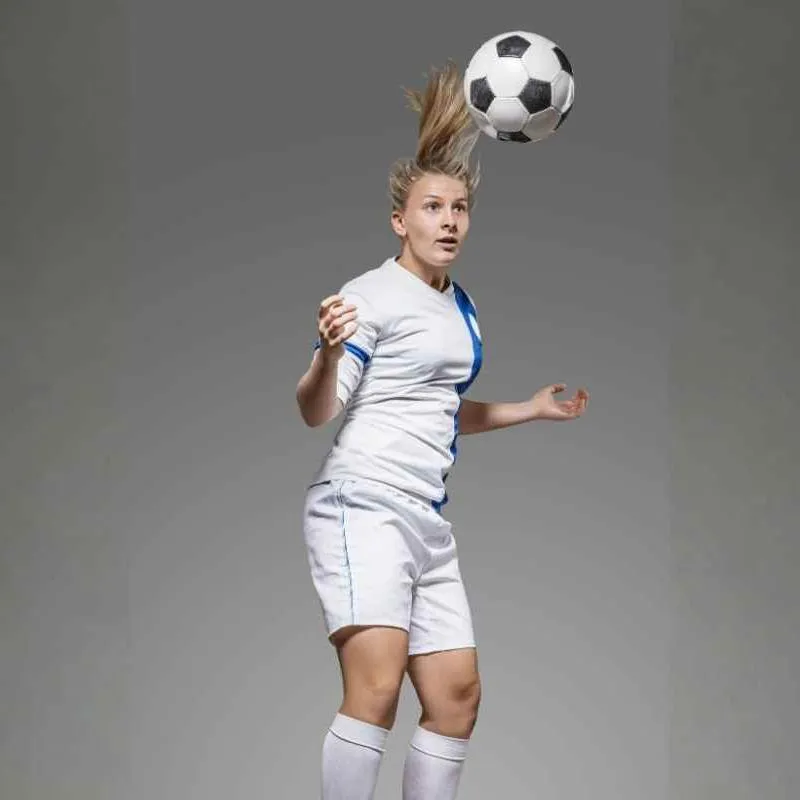 Fussballerin in weißem Trikot, Hose und Stutzen, köpft den Ball.
