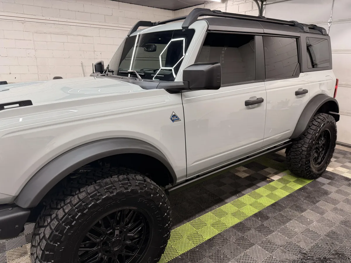 White SUV with off-road tires and black rims parked in a detailing shop, showcasing a polished exterior and luxury detailing environment.
