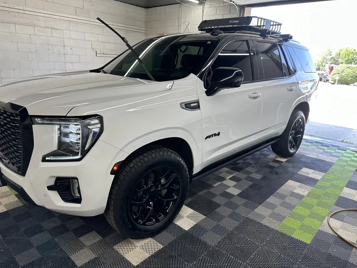 White GMC SUV in a detailing studio, showcasing a sleek exterior, black wheels, and roof rack, emphasizing luxury auto detailing and eco-friendly practices.
