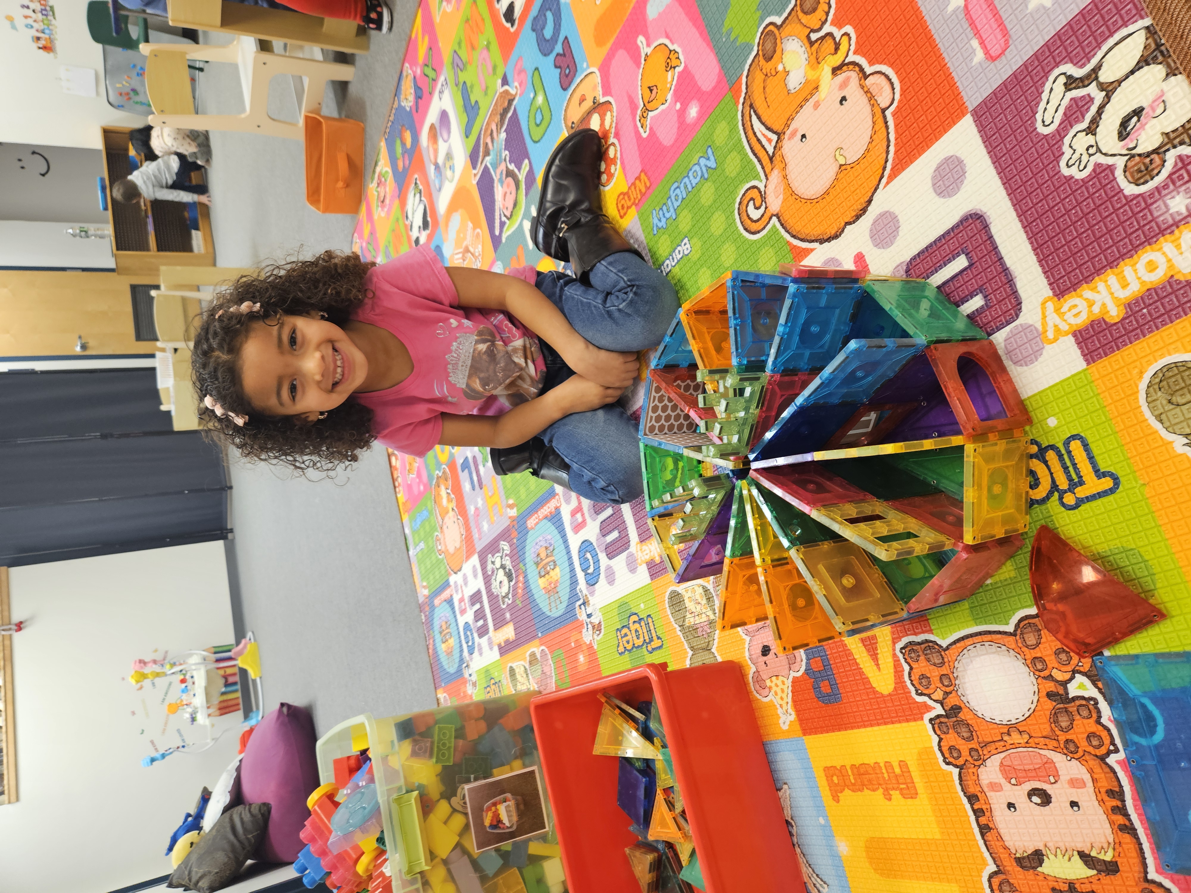 Three-year-old girl mid-jump in a playful preschool scene, energetic and smiling.