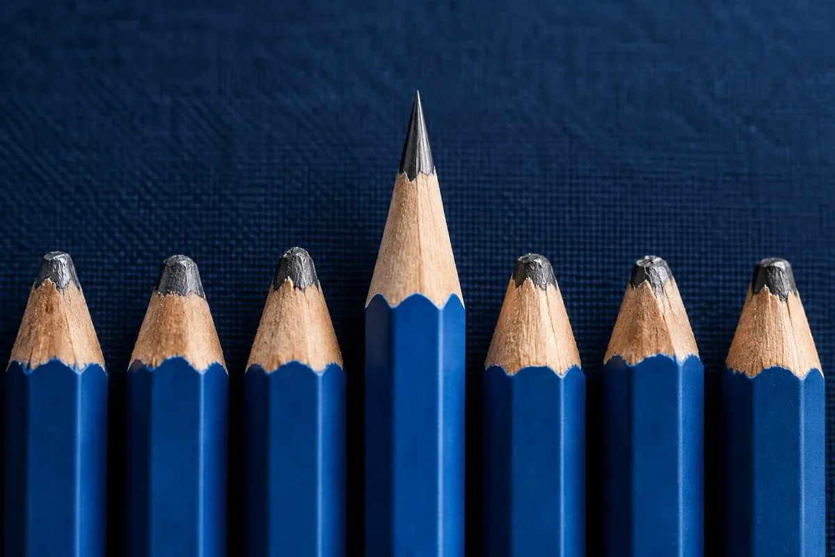 One carefully sharpened pencil among a row of blunt pencils, precision macro shot on dark navy fabric, clear single-point metaphor.
