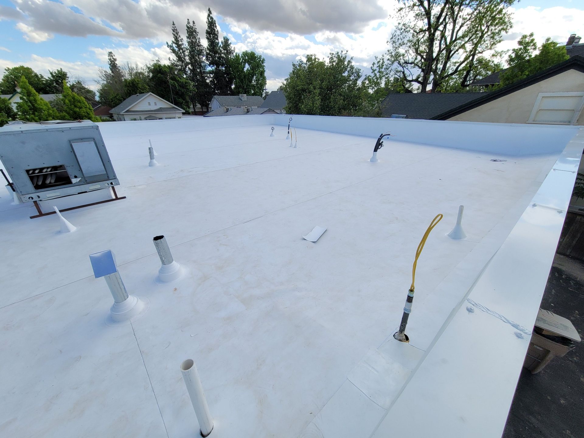 Finished white TPO flat roof with sealed pipe flashings and a rooftop HVAC unit in Bakersfield