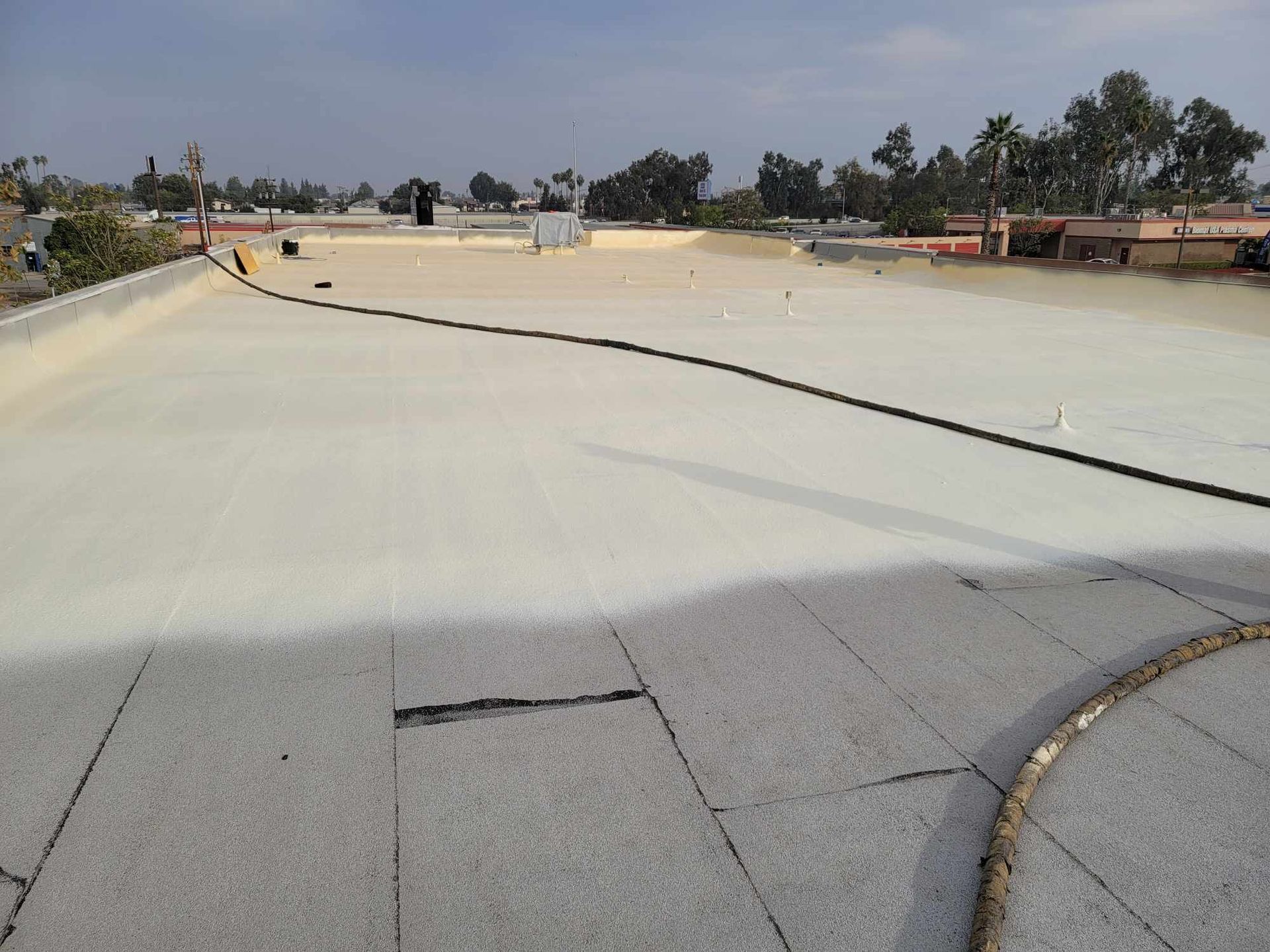 Old cracked flat roof seams next to fresh spray foam on a commercial building