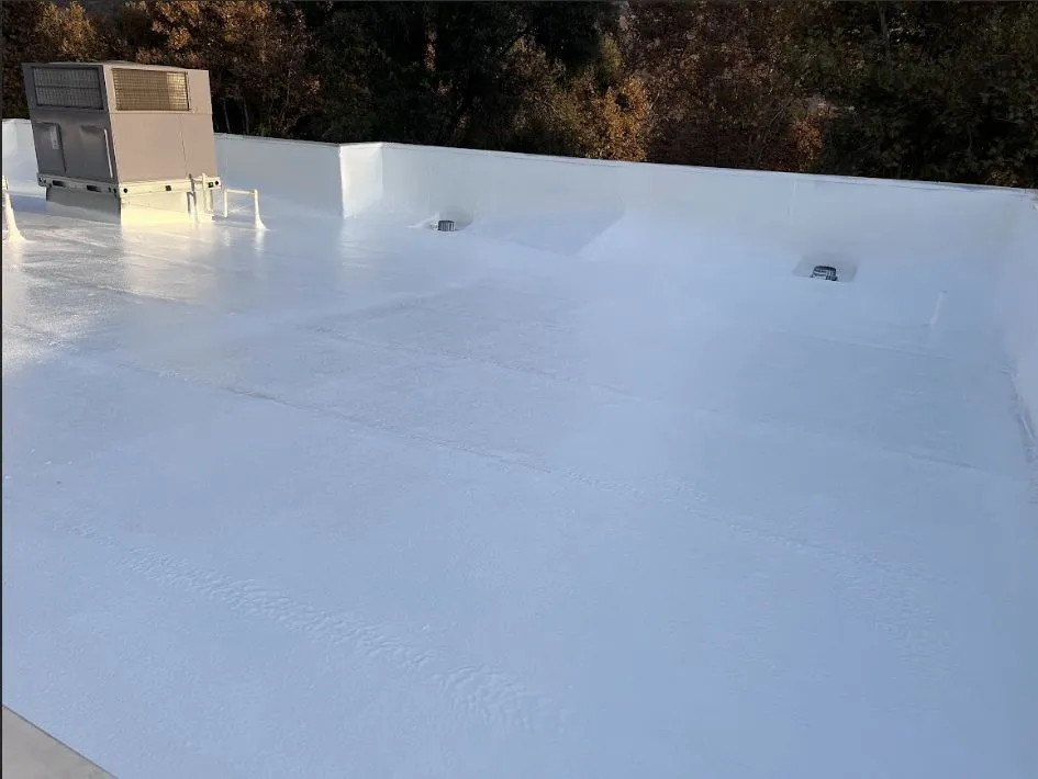 White reflective coating on a flat commercial roof with a rooftop HVAC unit and parapet walls