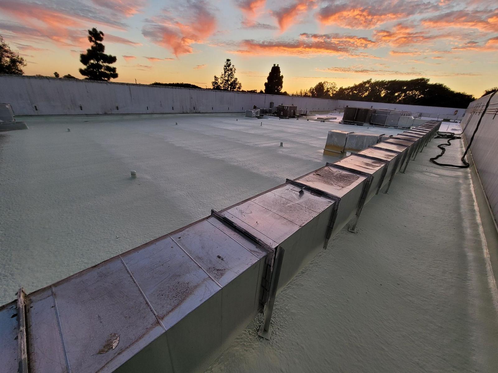 Newly sprayed foam roof on a large Bakersfield commercial building at sunset, with rooftop ductwork