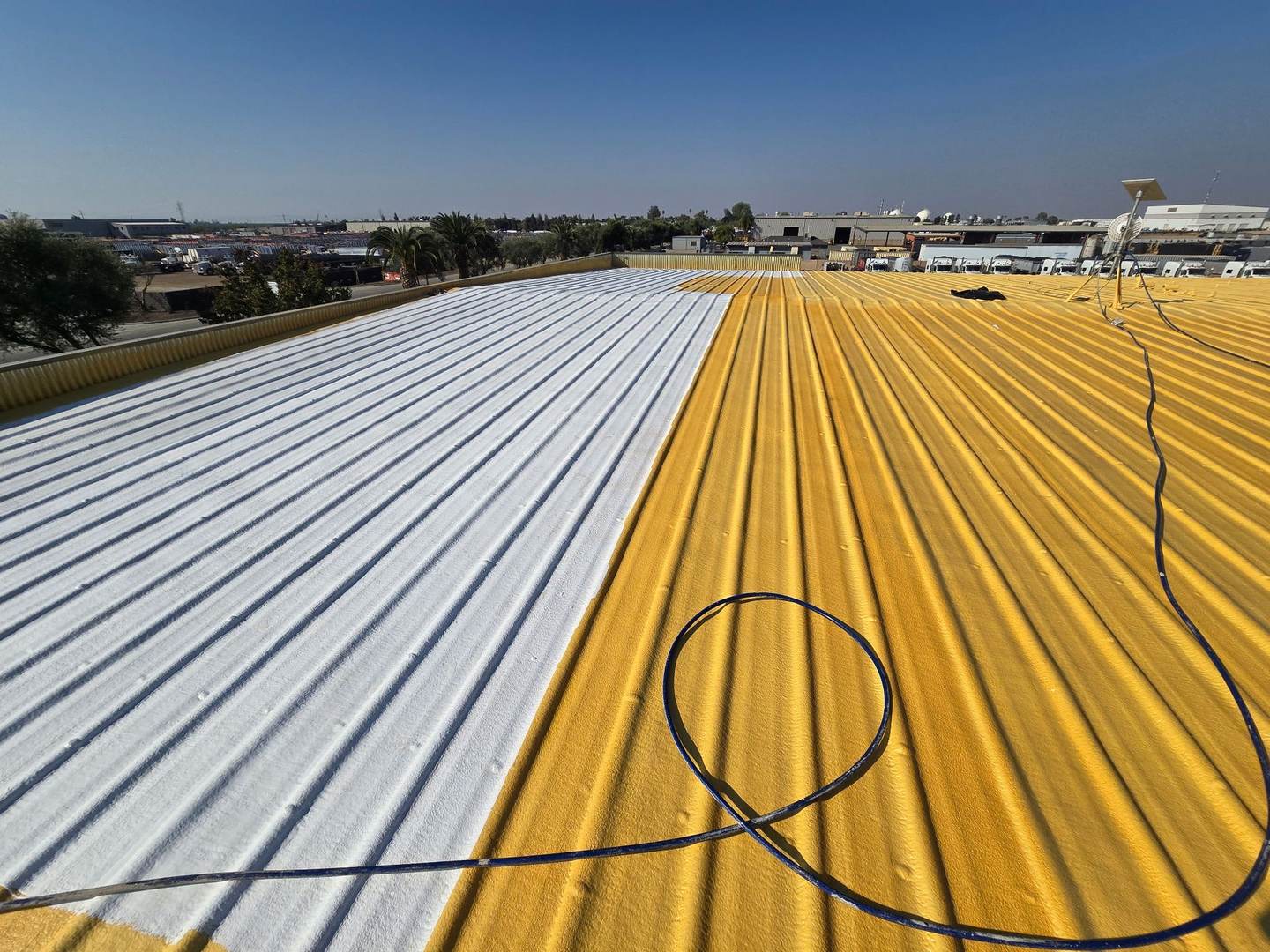 Metal roof on a Bakersfield commercial building, half covered in yellow spray foam and half finished with white coating