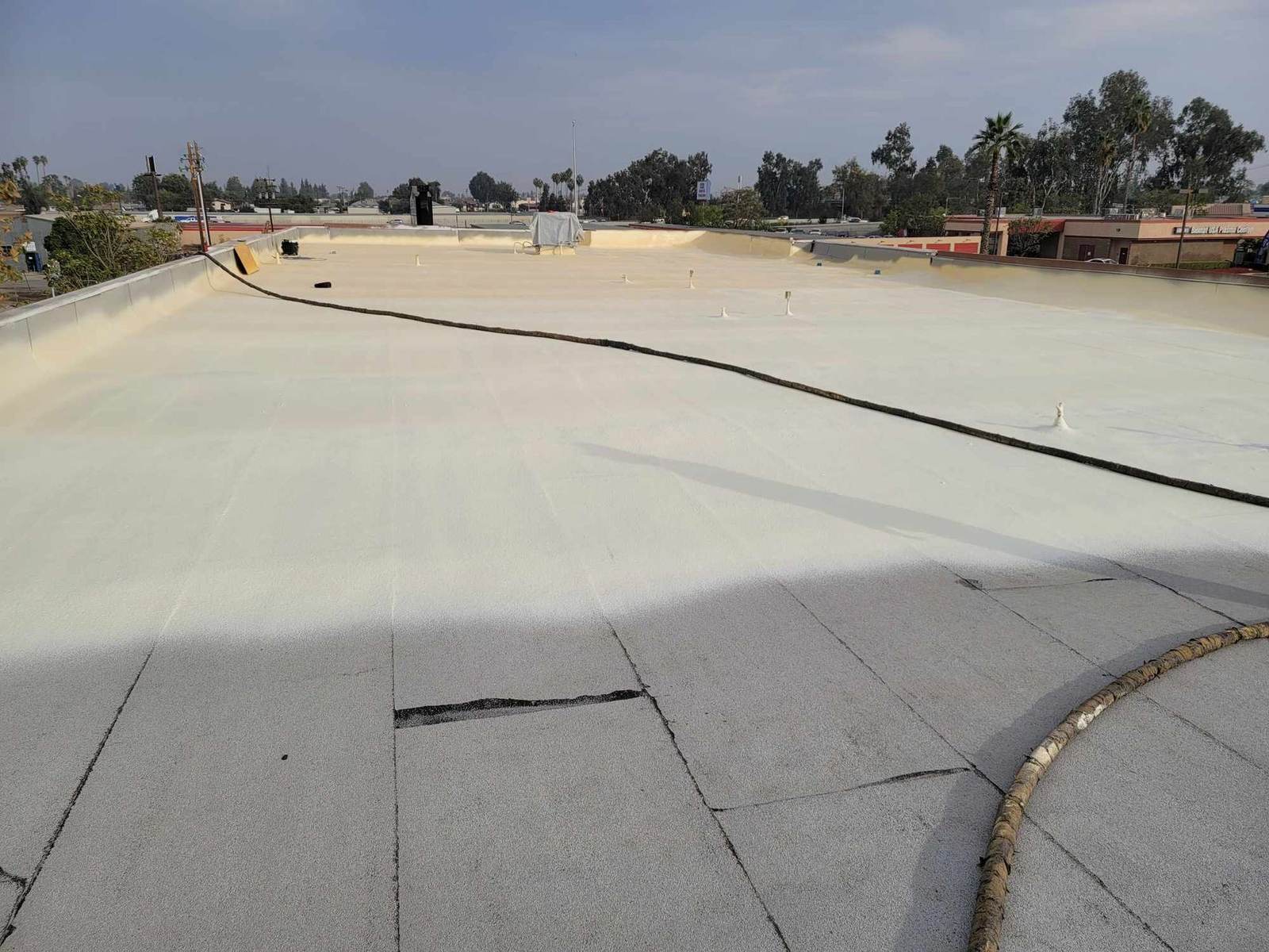 Cracked, aging flat roof being covered with new spray foam on a Bakersfield commercial building