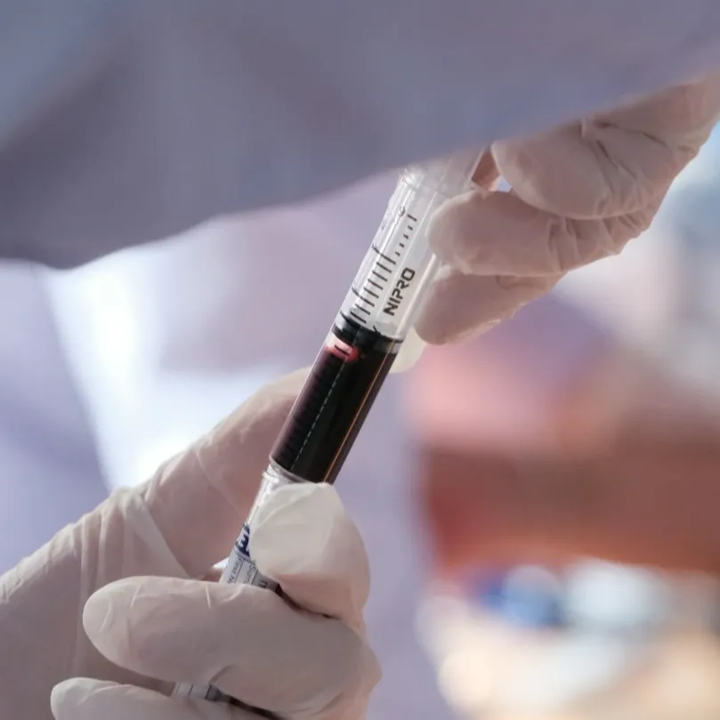 Close up gloved hands of lab tech holding vial of blood