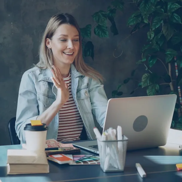 Woman sitting at desk with computer, waving at screen