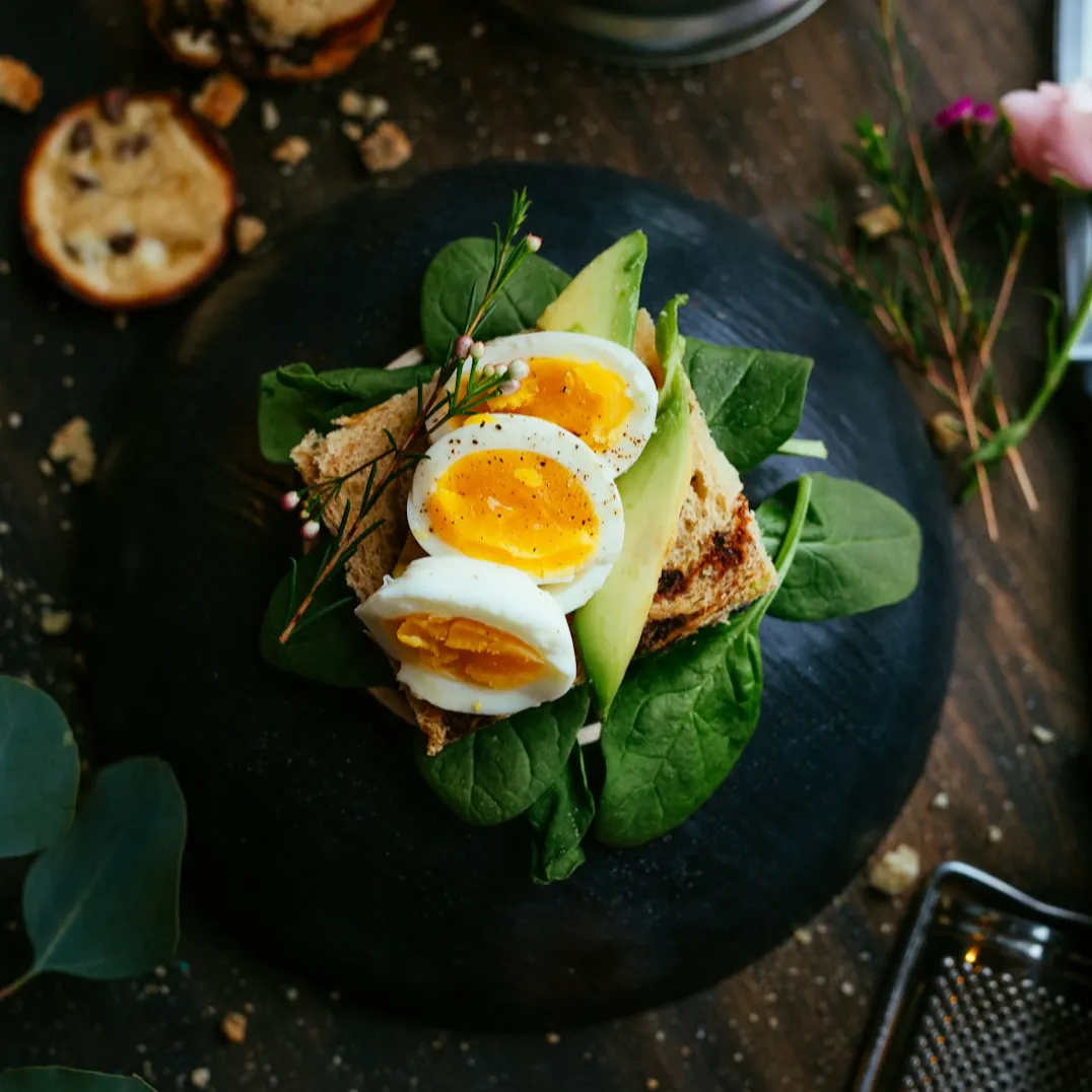 Stylistic black plate with spinach and avocado toast with hardboiled eggs