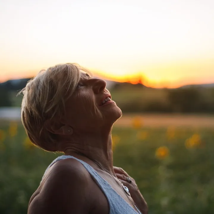 Older woman looking up at sky in hope with blurred mountains in background