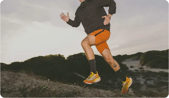 Man wearing a dark jacket and orange shorts running outdoors on a sandy dune, representing enhanced energy and male physical performance.