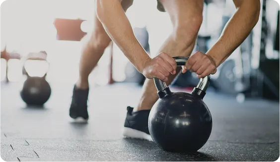 Close-up of a man performing an exercise with a black kettlebell on a gym floor, symbolizing men's strength, fitness, and physical well-being.