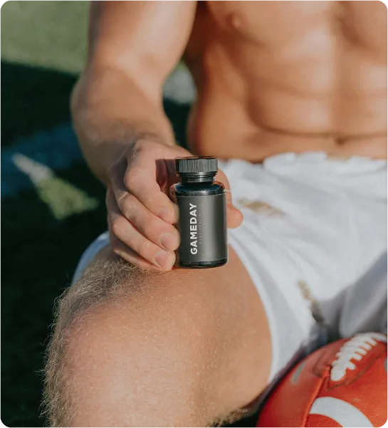 Muscular man in white shorts holding a small black bottle labeled 'Gameday' near a football, representing male performance and supplemental health support.