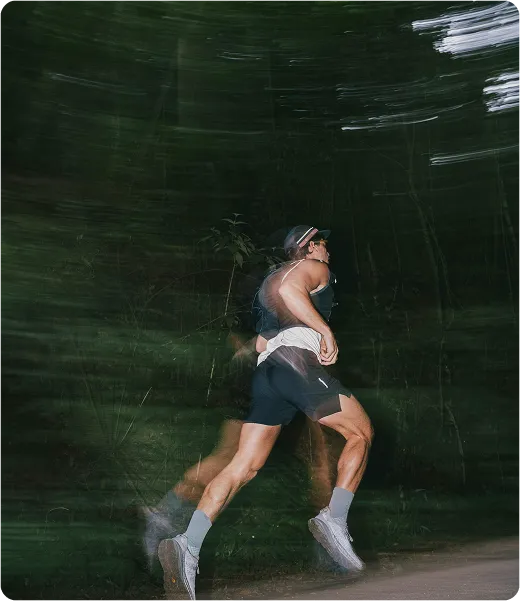 Man running fast on a trail at night, captured with motion blur to convey high energy, endurance, and peak male physical vitality.
