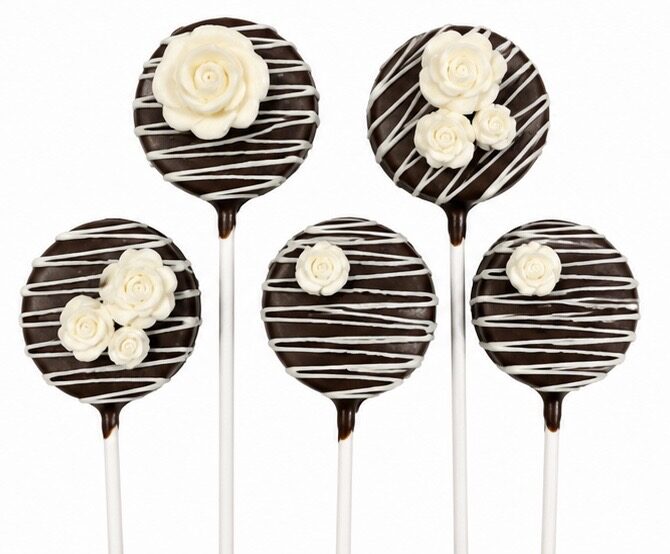 Chocolate cake pops decorated with white chocolate drizzle and edible rose accents, by Sugar Coast Sweets