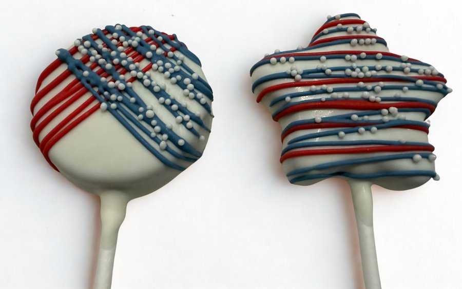 White chocolate cake pops striped red and blue with silver sprinkles, a patriotic Fourth of July design by Sugar Coast Sweets
