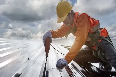 Technician fastening metal roofing panels with drill for Coon Rapids Commercial Roofing