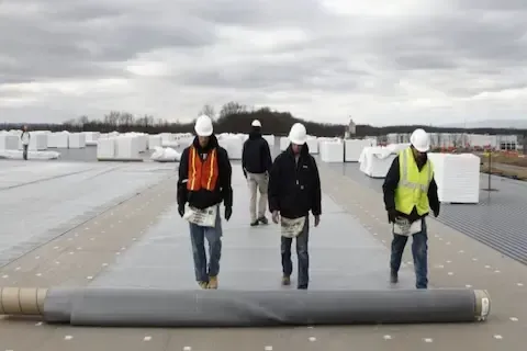 Commercial roofing crew unrolling membrane across flat roof in Coon Rapids