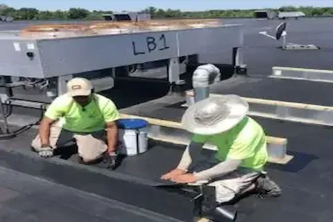 Two workers repairing flat roof surface near rooftop HVAC equipment in Coon Rapids