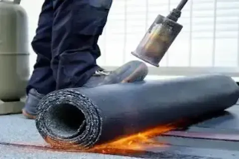 Open flame torch applied to rolled modified bitumen membrane during flat roof installation in Coon Rapids