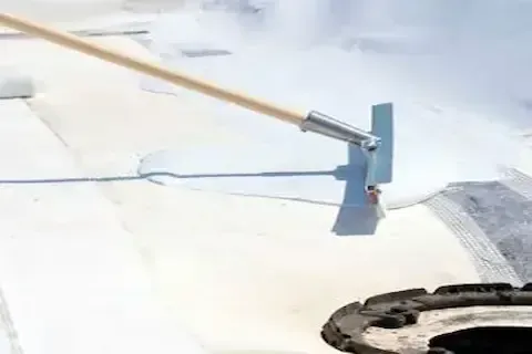 Liquid roof coating spread across flat commercial rooftop with a long-handled squeegee