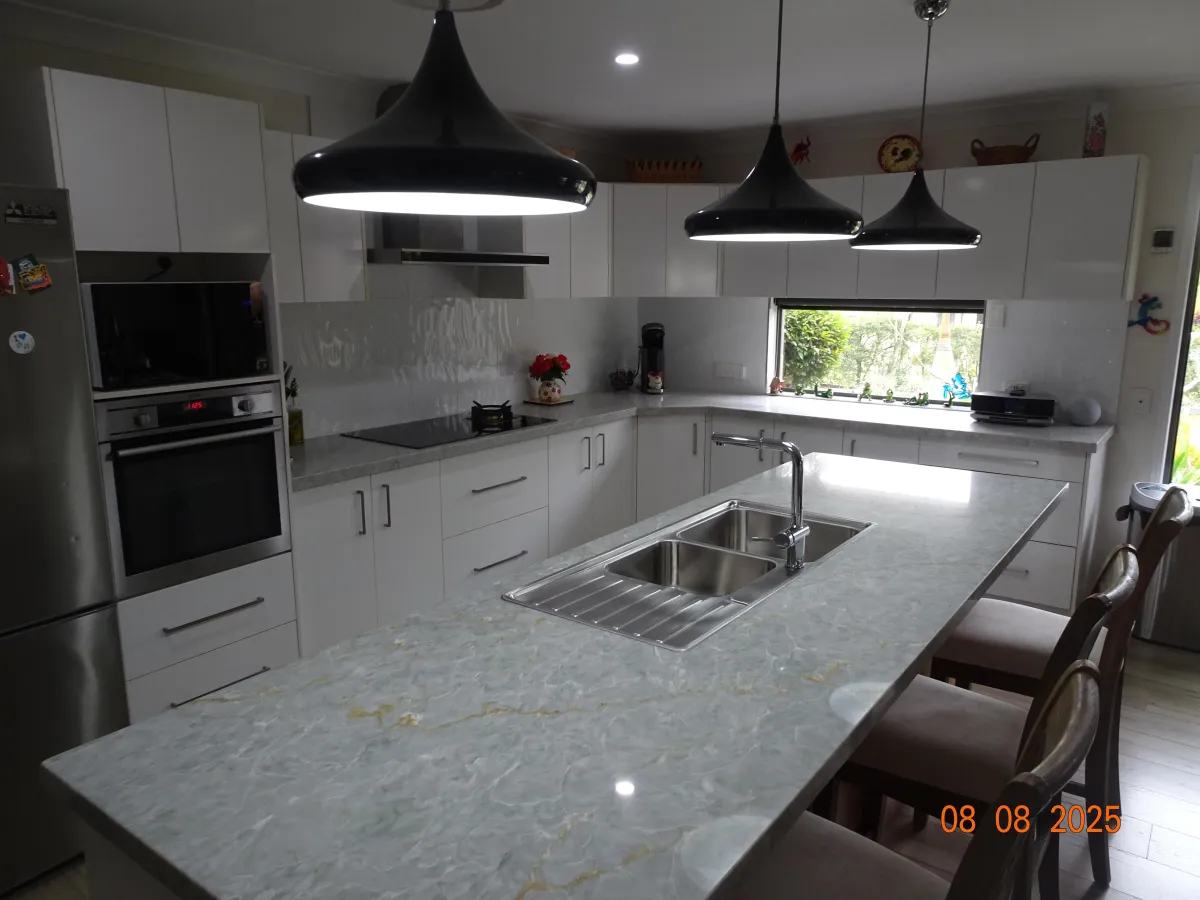 Modern kitchen with polished jade green marble countertops featuring subtle gold veining, white cabinetry, and black pendant lighting, showcasing the Jade Ember Counter Surface’s elegant natural tone.