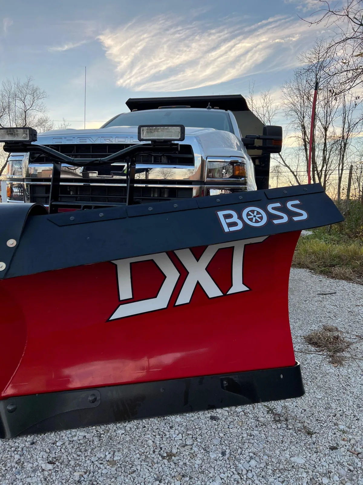 Heavy-duty snow plow attached to a large truck, clearing a commercial lot, midday, snow piles visible, industrial setting, 1:1 aspect ratio.