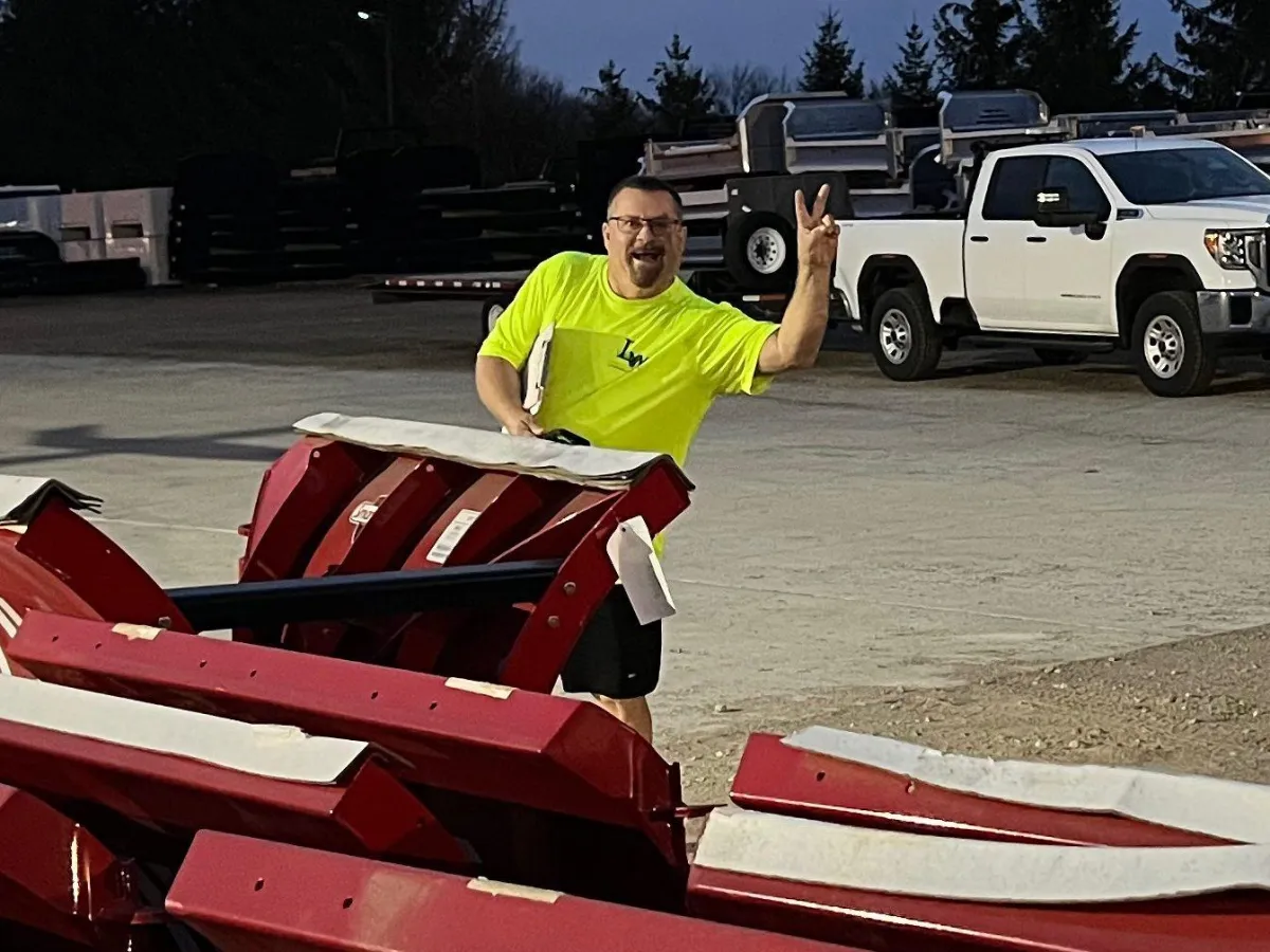 LW Snow Supply team group photo, diverse staff in branded winter gear, standing in front of company vehicles, cheerful expressions, snowy background, 3:2 aspect ratio.