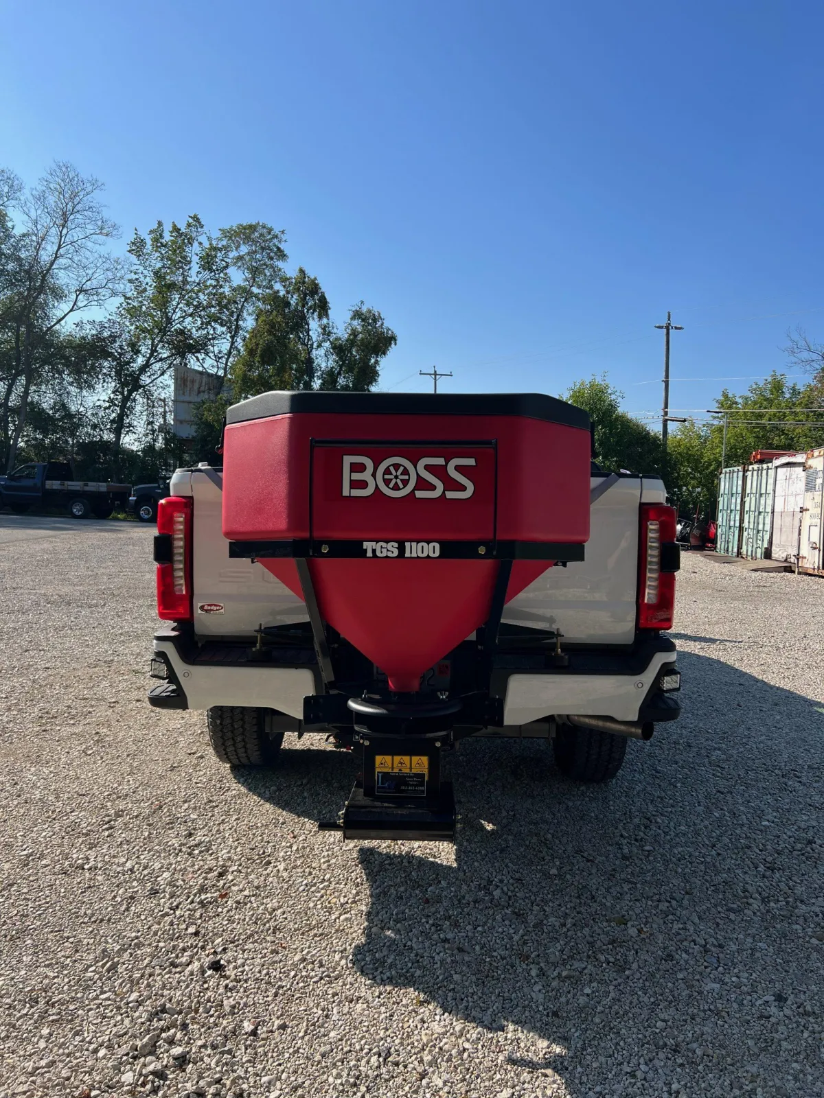 Compact snow plow machine parked on a suburban driveway, early morning, light snow on the ground, blue and silver finish, 1:1 aspect ratio.