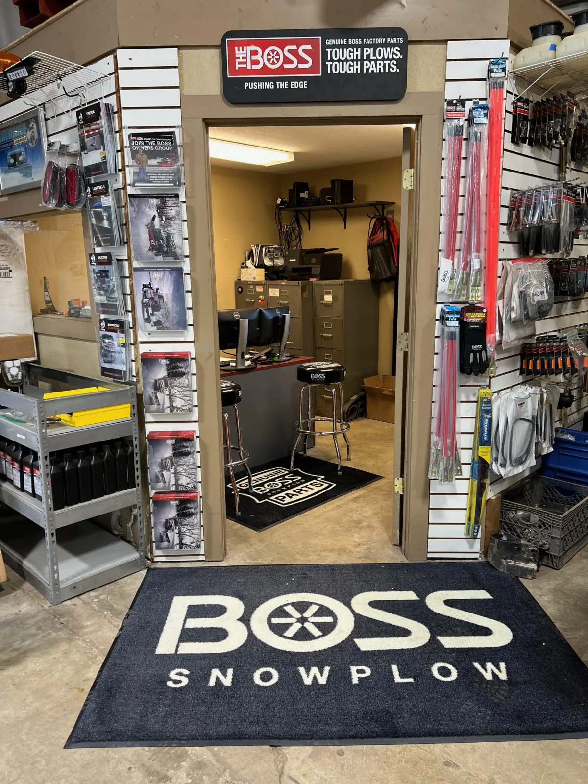 Multi-purpose snow plow with adjustable blade, parked beside a small business storefront, afternoon, clear sky, 1:1 aspect ratio.