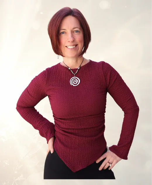 Kirstin Carey kneeling outside, smiling while petting her dogs — relaxed, grounded, and at home in her energy.