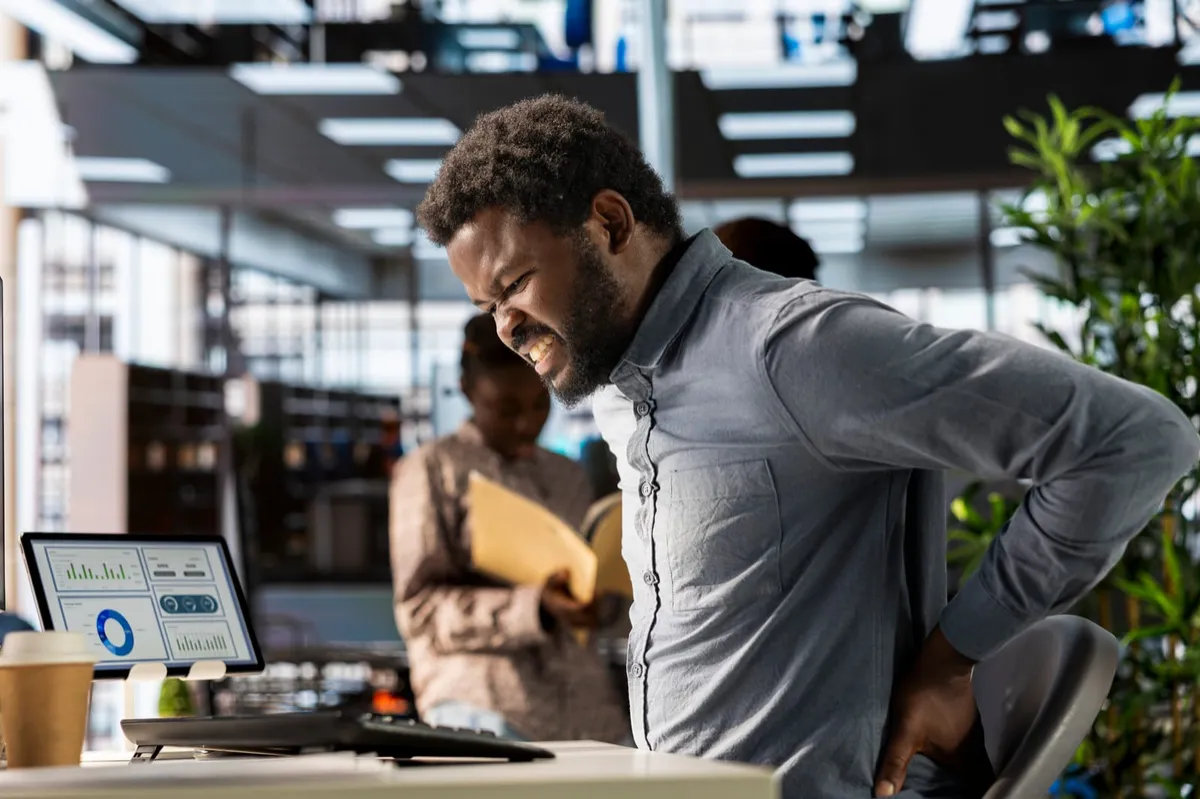 Man holding his lower back while returning to work after a back pain flare-up