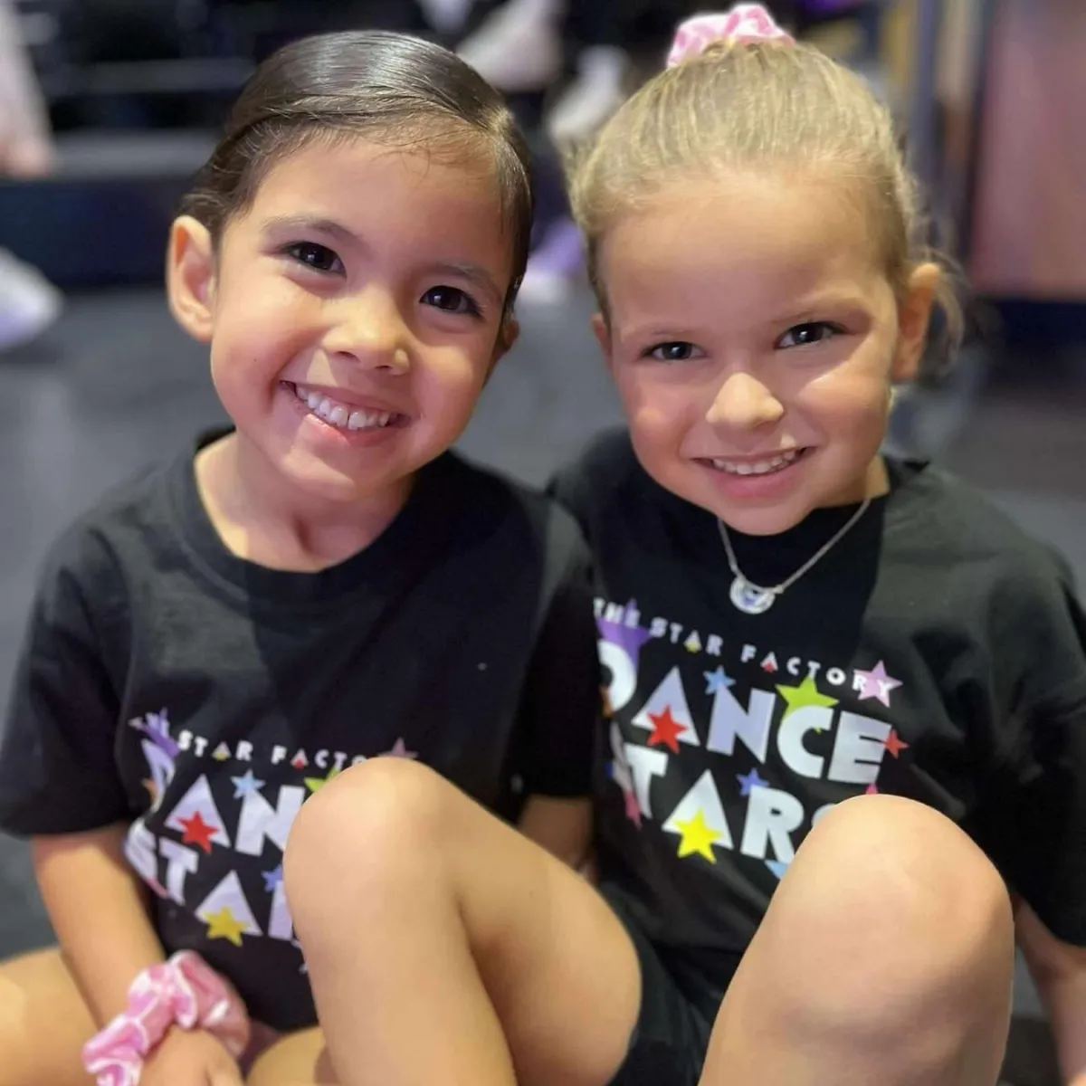 Two young adorable girls smiling in Star Factory Dance Stars uniforms at Joondalup's leading kids dance studio, showcasing fun and friendship in children's dance classes.
